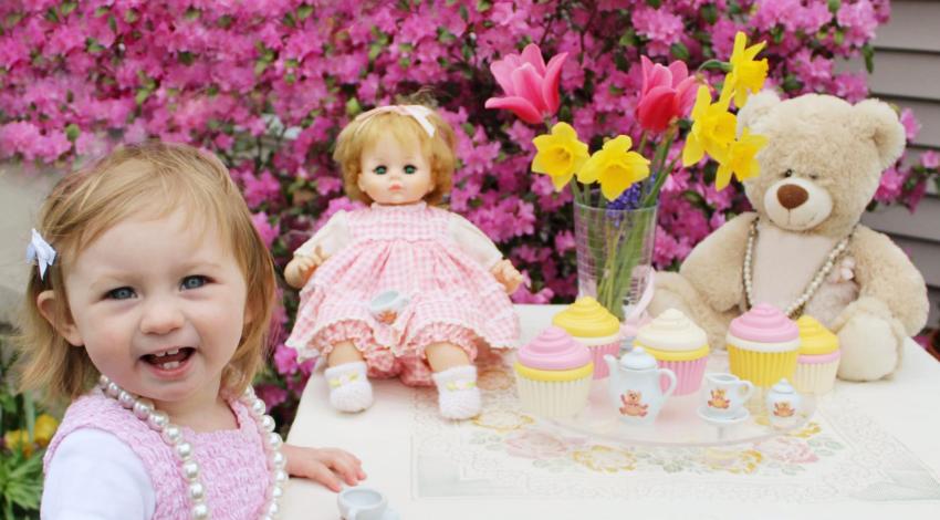 little girl at table with tea set, doll and teddy bear