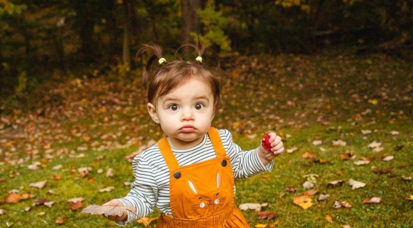 little girl in orange dress in front of fallen leaves