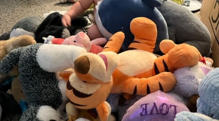 laughing baby sitting on floor, surrounded by stuffed animals