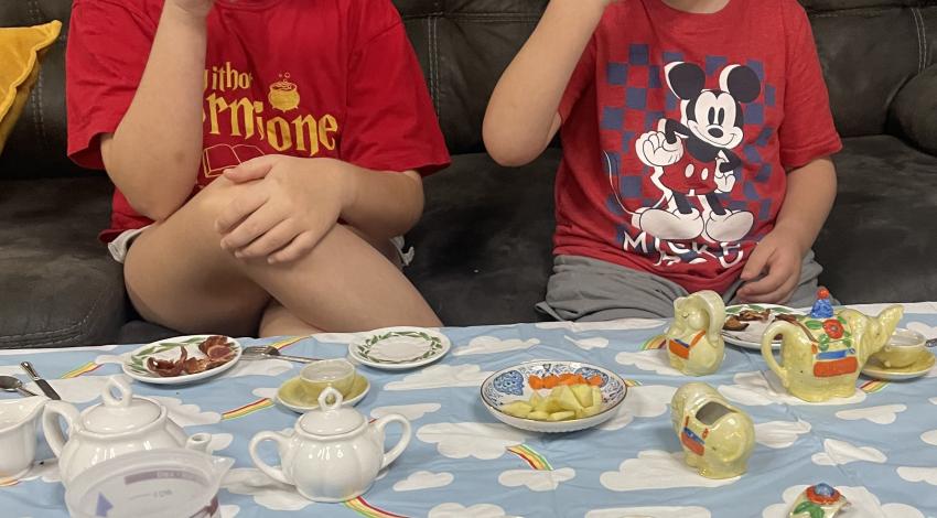 boy and girl sip tea behind table set with china teacups and teapot