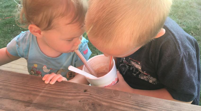 Toddler and baby sip milkshake through straws