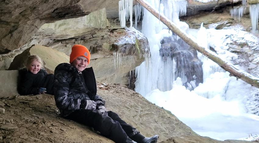 boy and girl sitting in front of frozen waterfall