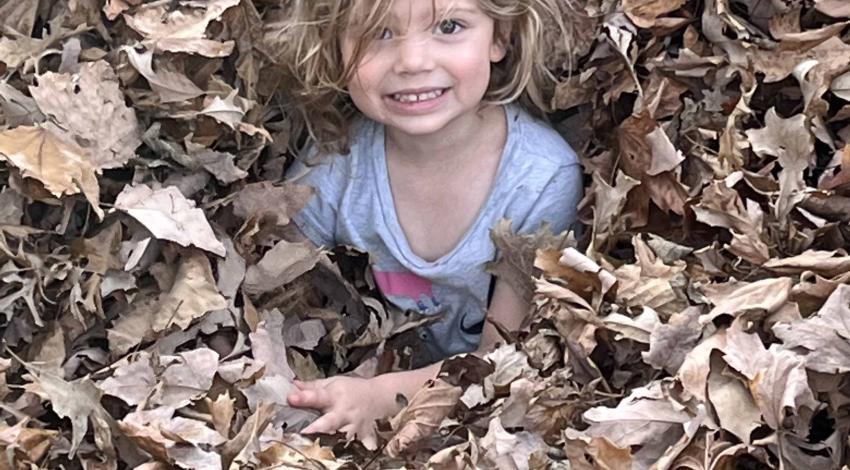 smiling child sits chest-deep in leaf pile