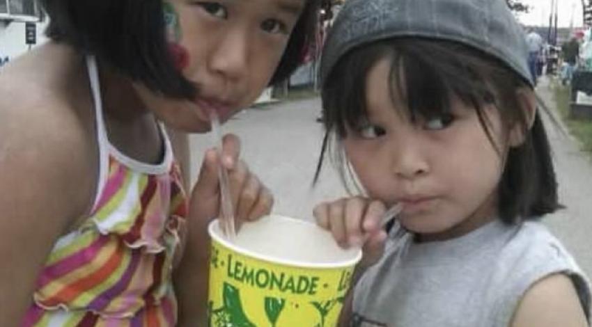 Two girls sip through straws from large cup of lemonade