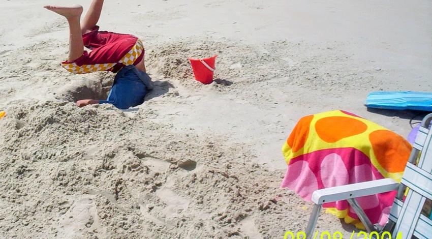 boy's legs stick out from hole in sand