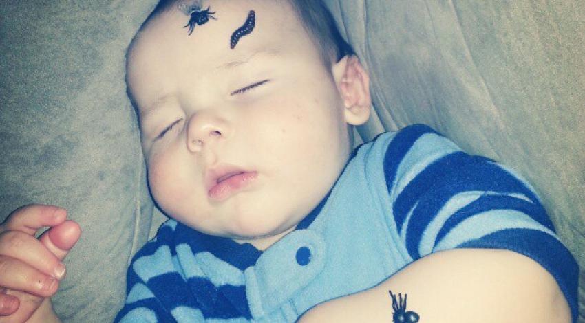 baby sleeping with black spider stickers on his arm and forehead