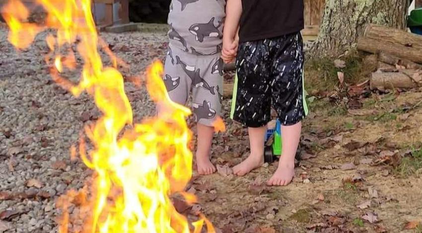 two boys stand behind blazing campfire