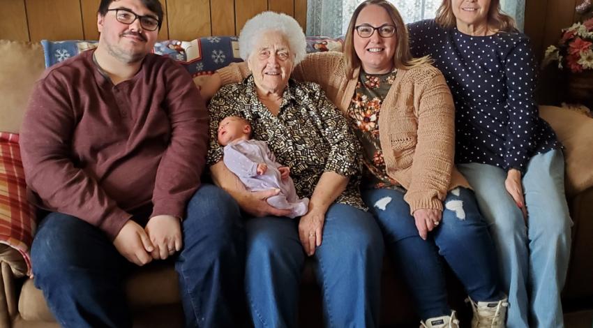 three women, a man, and a small baby on a couch