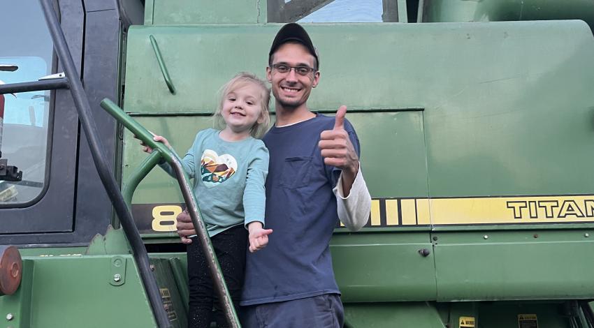 man and small girl in front of green farm machinery