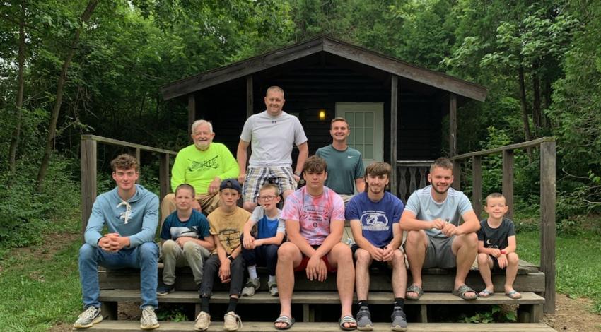 About a dozen people sitting and standing on steps in front of a cabin