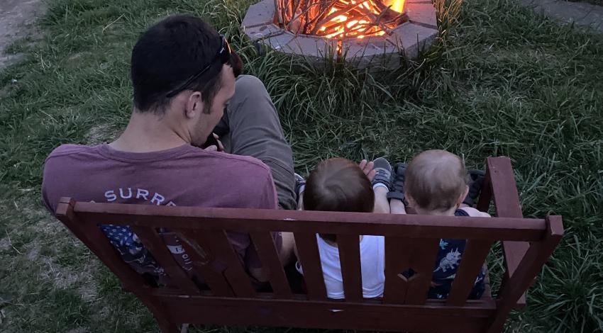 man with two small children on bench by campfire