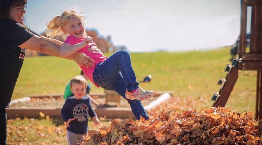 woman tossing little girl into leaf pile