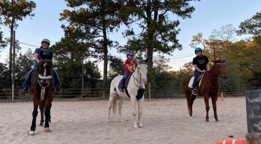 three people on horseback in riding arena