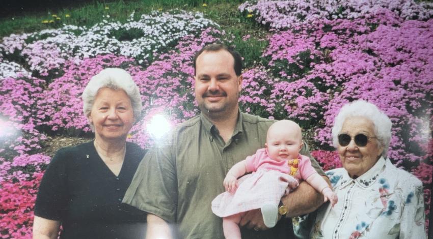 three adults and a baby in front of flower beds