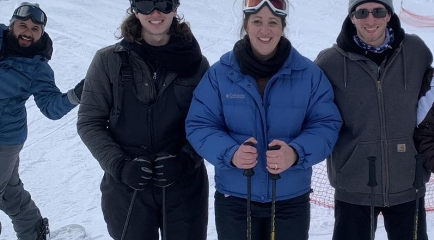 three skiers posing, with photobomber behind