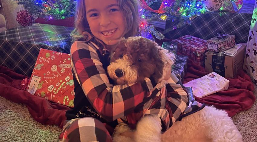 girl hugging dog in front of Christmas tree