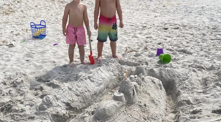 two boys standing behind sandcastle