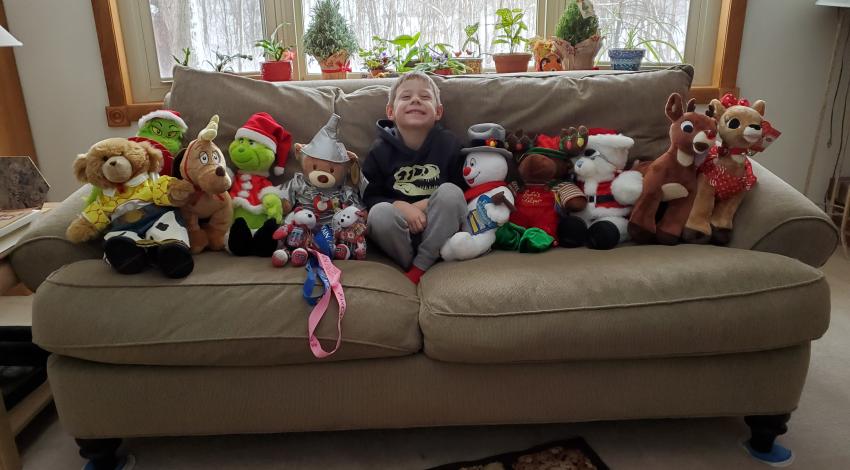 Small boy on couch, surrounded by Christmas-themed stuffed animals