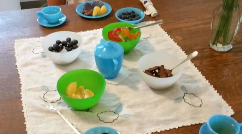 girl sitting behind table set with blue tea set, including cups of tea and fruit on plates