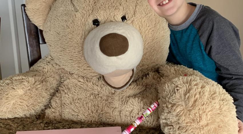 Little boy sitting next to giant stuffed bear
