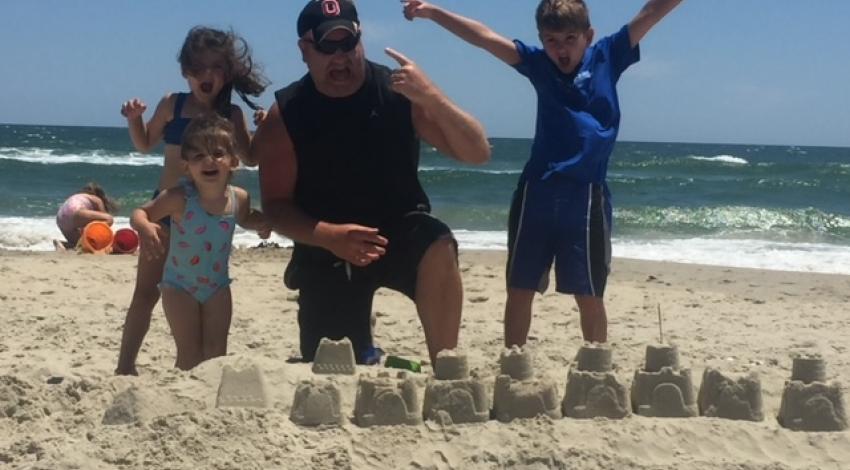 man and three children behind sandcastle