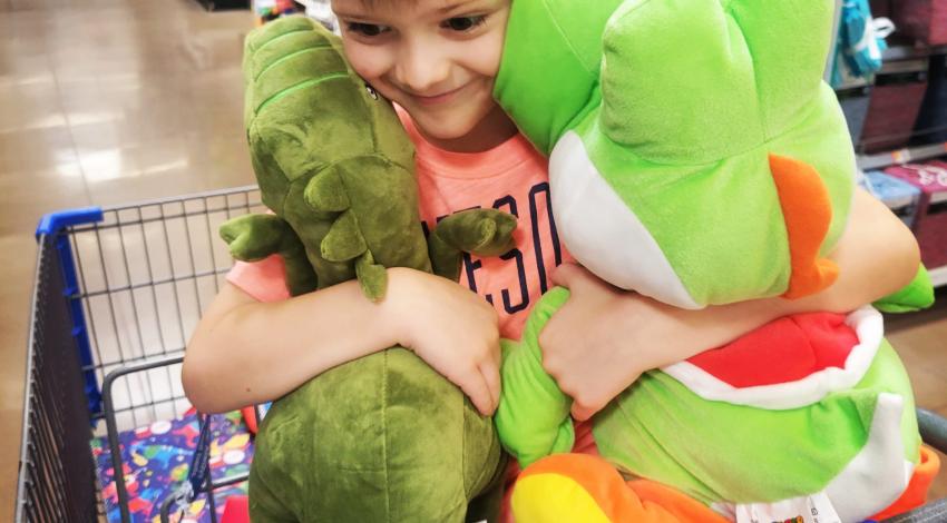 young boy in shopping cart hugging two stuffed animals
