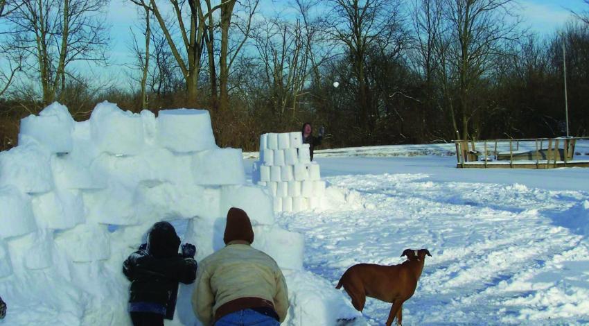 man and boy hiding behind wall of snow