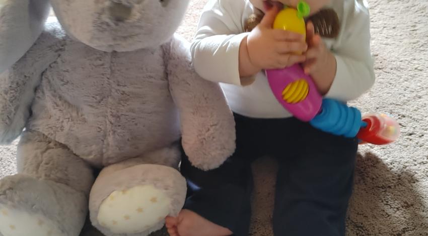 Baby sitting next to gray stuffed bunny
