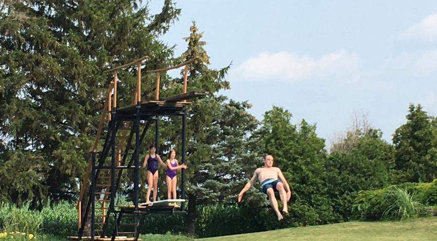 people jumping off diving board into pond