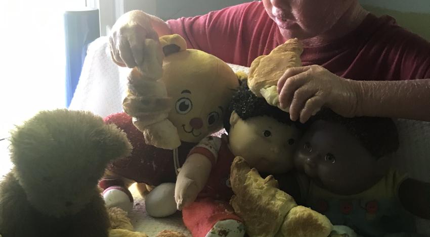 little boy in red hat shares croissants with teddy bears and dolls