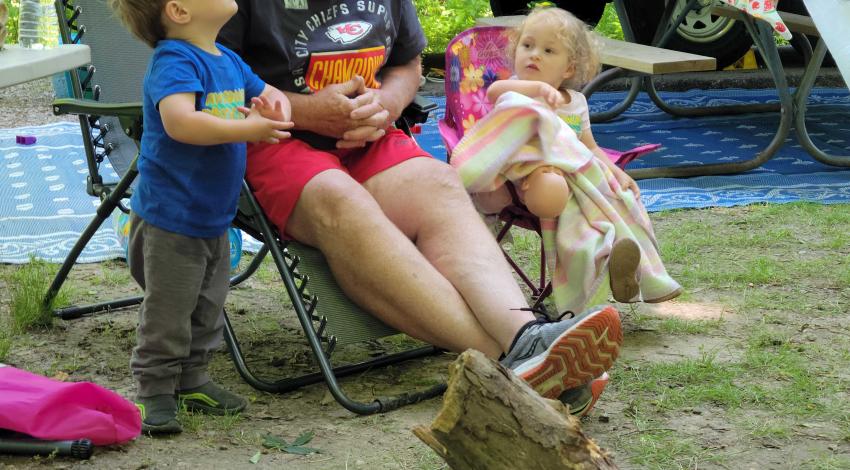 man and two small children looking upward behind campfire