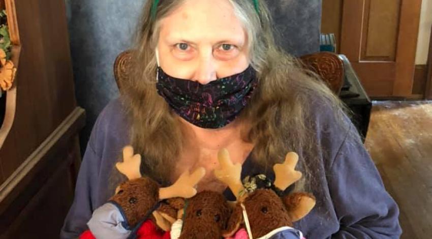 Woman wearing red antler headband, holding three stuffed reindeer
