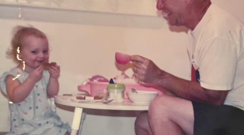 little girl sits at table with tea set, across from smiling man