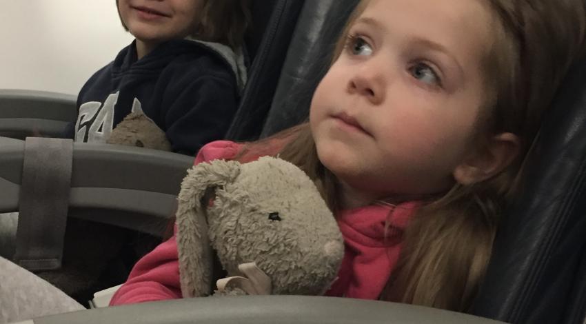 Small girl holding stuffed bunny in airplane seat with boy in next seat