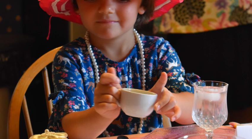 little girl with red hat and pearls, holding a teacup
