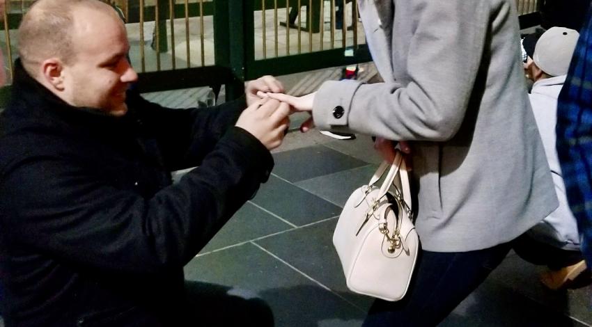 man kneeling in front of woman, putting ring on her finger