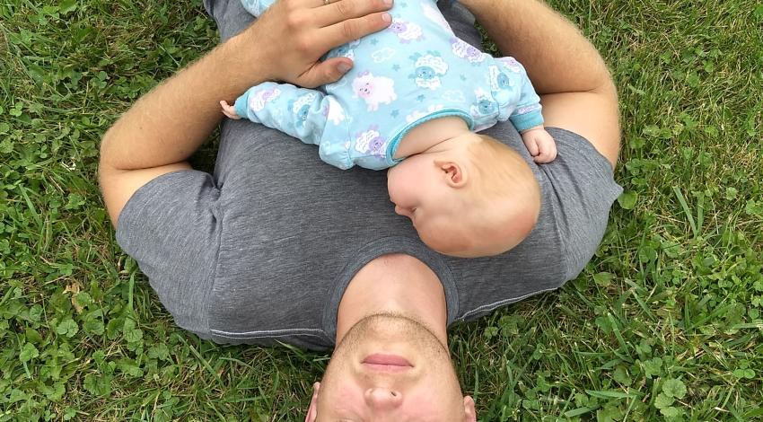 man sleeping on grass with baby on his chest