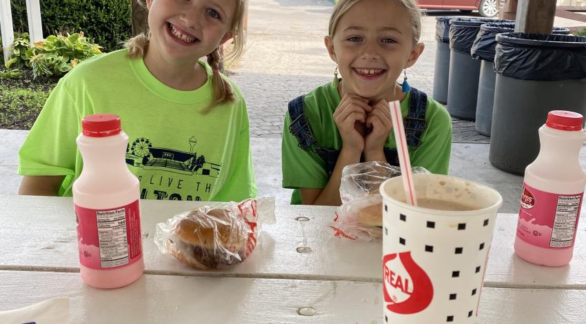 Two smiling girls behind table with food.