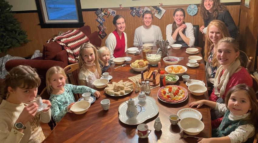 children and adults sit around a large table set for tea