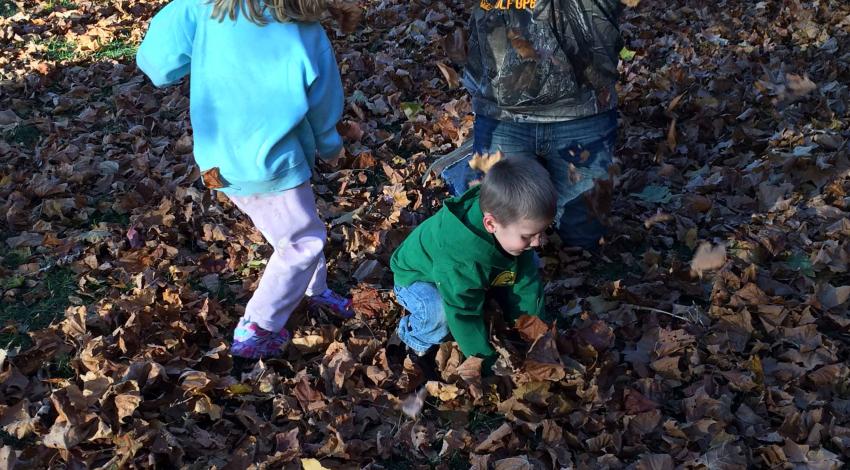 two children and a man toss leaves in leaf pile