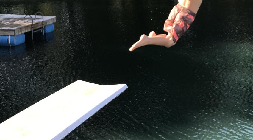 little boy leaps off board into lake