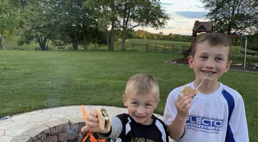 two boys in baseball uniforms eating s'mores by fire