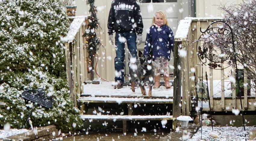 two kids and dog on porch with snow falling