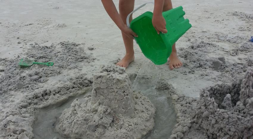 girl adds water to sandcastle moat