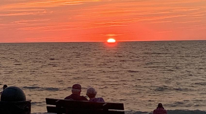 couple sits on bench watching sunset 