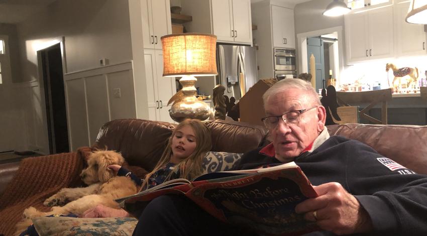 Man reading to girl, with dog on couch