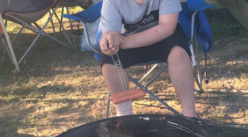 boy smiles while cooking hot dog over a campfire