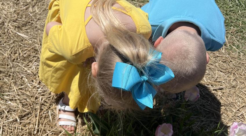 little girl and little boy, bending over to smell flowers