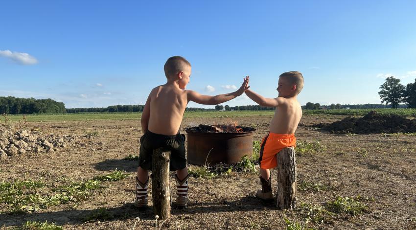 two boys give a high five in front of a campfire