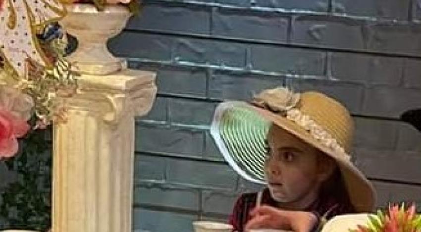 girl in pink sun hat enjoying a cup of tea
